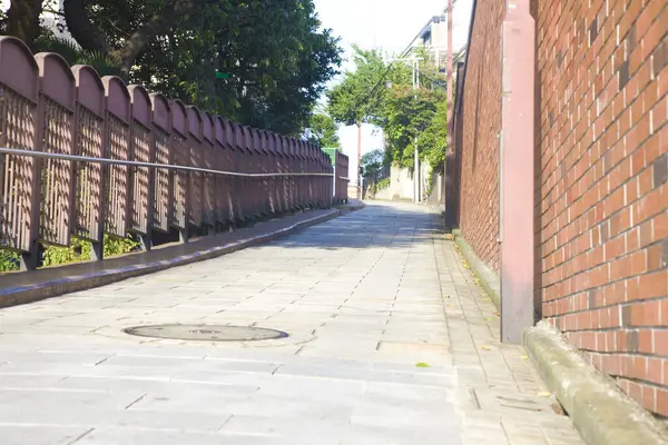 Tuğla duvar ve metal korkuluklardan oluşan güneşli boş bir sokak.