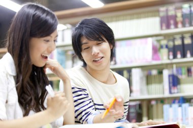 İki genç Asyalı üniversite öğrencisi kütüphanede okuyor. 