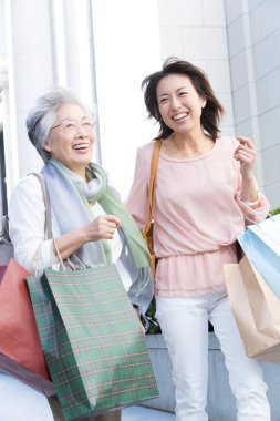 İki kadın alışveriş torbalarıyla kaldırımda yürüyorlar.