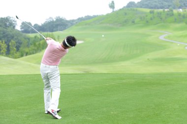 Golf sahasında golf topuna vuran bir golfçü.