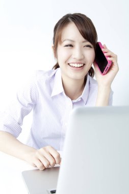 Laptop kullanan ve akıllı telefondan konuşan genç bir kadın. 