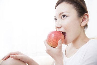 Genç Asyalı kadın evde elma yiyor. 