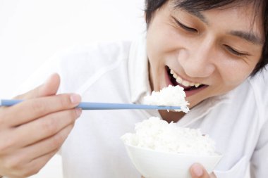 Genç Asyalı adam çubuklarla pilav yiyor. 