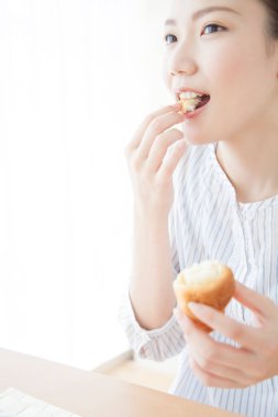 Asyalı kadın kahvaltı yapıyor, kek yiyor. 