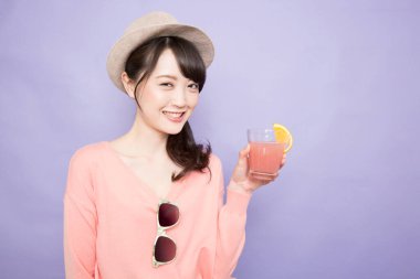 Bir bardak taze meyve suyuyla şapkalı güzel Asyalı kadının stüdyo fotoğrafı.