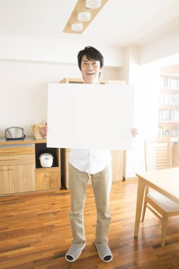 Evde boş beyaz tabela tutan bir adam var. 