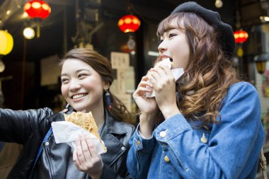 İki genç kadın markette abur cubur yiyor.