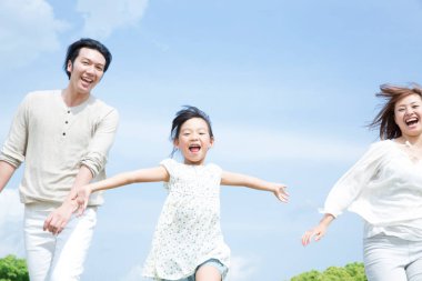 Mutlu Asyalı aile parkta eğleniyor, birlikte zıplıyorlar.