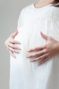 Karnının üstünde el ele tutuşan hamile kadının portresi..