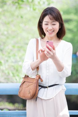 Genç ve güzel Asyalı kadın açık havada cep telefonu kullanıyor.