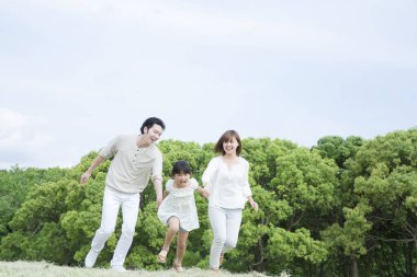 Mutlu Asyalı aile parkta eğleniyor, birlikte zıplıyorlar.