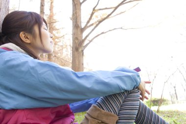 Sarı sırt çantalı genç Japon kadın sonbahar parkında yürüyüş yapıyor.