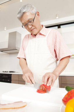 Asyalı son sınıf öğrencisi mutfakta domates kesiyor.