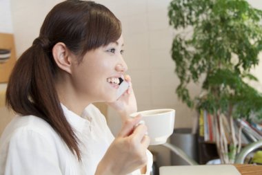 Genç bir kadın bir fincan kahve içiyor ve akıllı telefondan konuşuyor. 