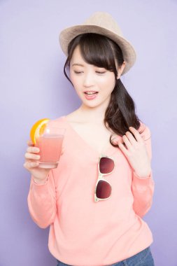 Bir bardak taze meyve suyuyla şapkalı güzel Asyalı kadının stüdyo fotoğrafı.