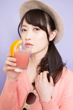 Bir bardak taze meyve suyuyla şapkalı güzel Asyalı kadının stüdyo fotoğrafı.