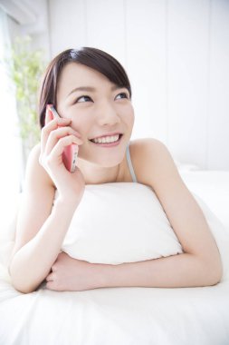 Kadın cep telefonu kullanarak yatakta yatıyor.