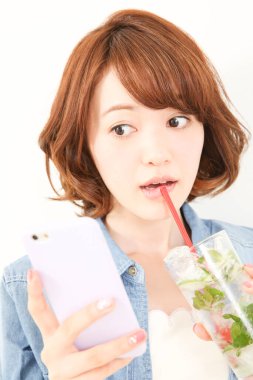 Güzel genç Japon kadının portresi ferahlatıcı bir içecek içiyor ve telefon kullanıyor.