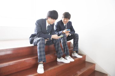 İki Asyalı okul üniformalı genç çocuk cep telefonu kullanıyor.