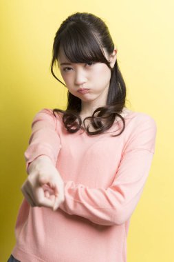 Asyalı üzgün bir kadın sarı arka planda dudaklarını büzüyor.