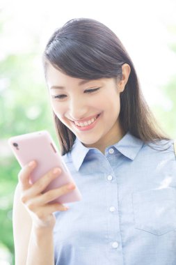 gülümseyen Asyalı kadın parkta akıllı telefon kullanıyor. 