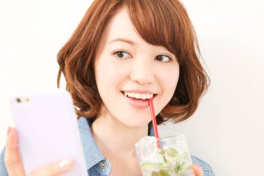 Genç Japon kadın limonlu ferahlatıcı su içerken elinde akıllı telefon tutuyor.