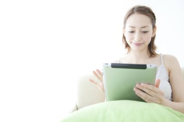 Kanepede tablet bilgisayarı olan genç Asyalı kadın. 