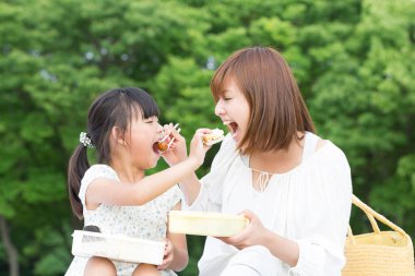 Anne ve kızı çimenlerde yemek yiyorlar. 