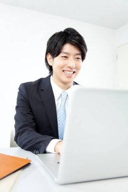 Genç Asyalı iş adamı ofiste dizüstü bilgisayarla çalışıyor. 