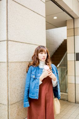 Akıllı telefonlu genç bir kadın duvarda duruyor.