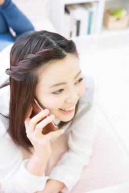 Asyalı kadın evde akıllı telefon kullanıyor.