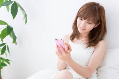 Asyalı kadın yatak odasında akıllı telefonuyla fotoğraf çekiyor. 