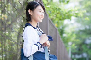 Gülümseyen Japon kız öğrenci üniforması içinde sokakta poz veriyor.