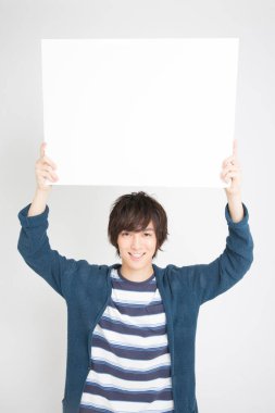 Asyalı adam beyaz arka planda boş bir ilan panosu tutuyor.