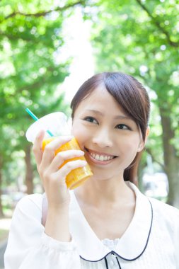 Sıcak yaz günü yanağında soğuk portakal suyu bardağıyla gülümseyen Asyalı kadının portresi.