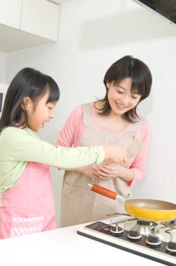 Gülümseyen Japon kadın ve kızı mutfakta yemek pişiriyor.