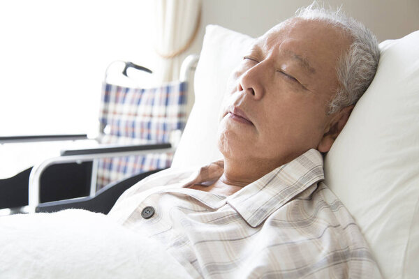 старший азиатский мужчина спит на кровати в больнице.