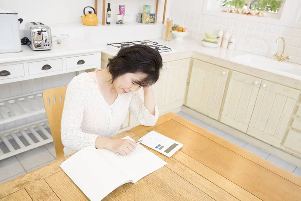 asian woman with calculator sitting  in the kitchen