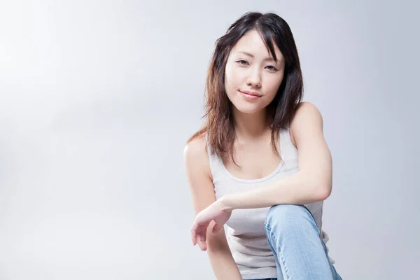 灰色の背景に白いシャツとジーンズが付いている美しい若いアジアの女性 ストック写真