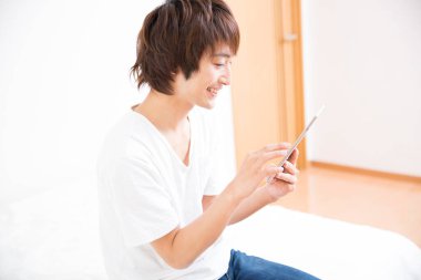 Kanepede tablet kullanan Asyalı bir adam.