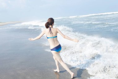 Mavi bikinili genç Asyalı kadın yaz plajında tatilin tadını çıkarıyor.