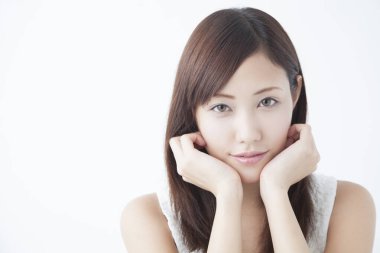 Genç, güzel Asyalı bir kadın. Yüzü asık, soyutlanmış arka planda poz veriyor.  