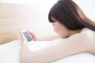 Genç Asyalı kadın yatakta uzanıyor ve cep telefonu kullanıyor..