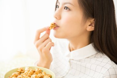 Güzel Asyalı genç kadın evde patlamış mısır yiyor.