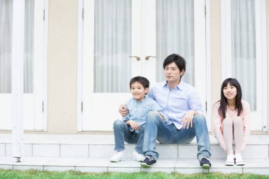 Genç Asyalı bir aile evinin merdivenlerinde oturuyor. 