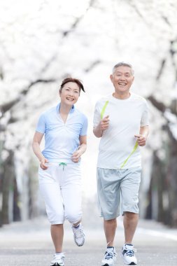 Parkta çiçek açan ağaçlarla koşan Asyalı olgun bir çift.