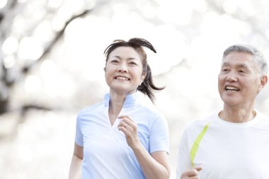 Parkta çiçek açan ağaçlarla koşan Asyalı olgun bir çift.