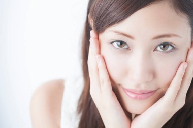 Genç, güzel Asyalı bir kadın. Yüzü asık, soyutlanmış arka planda poz veriyor.  