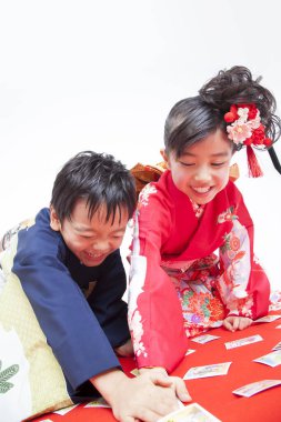 Geleneksel kıyafetli çocuklar yerde oturmuş kağıt oynuyorlar.