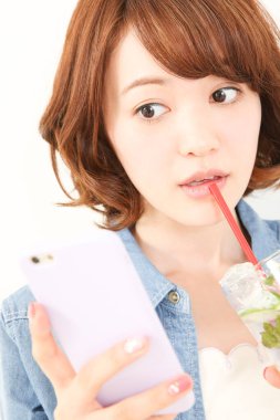 Güzel genç Japon kadının portresi ferahlatıcı bir içecek içiyor ve telefon kullanıyor.
